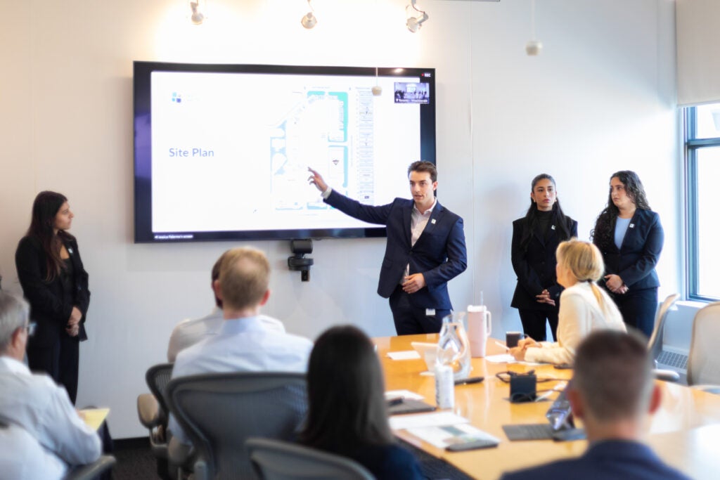 Intern presenting with group pointing at screen Infront of people at table