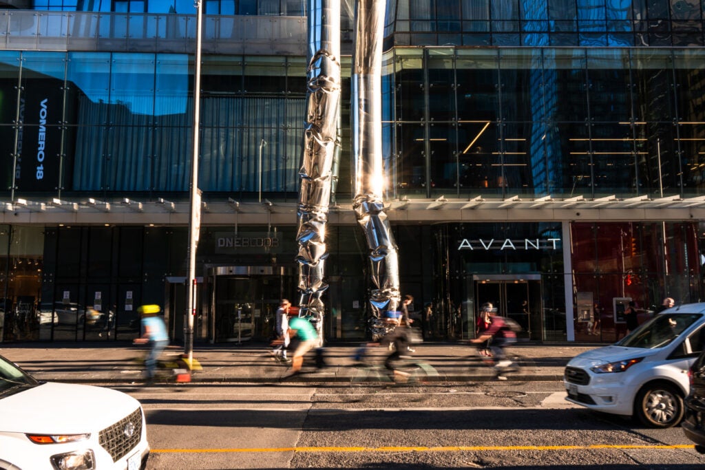Facade of Avant by Altea with cars, cyclists and people passing by
