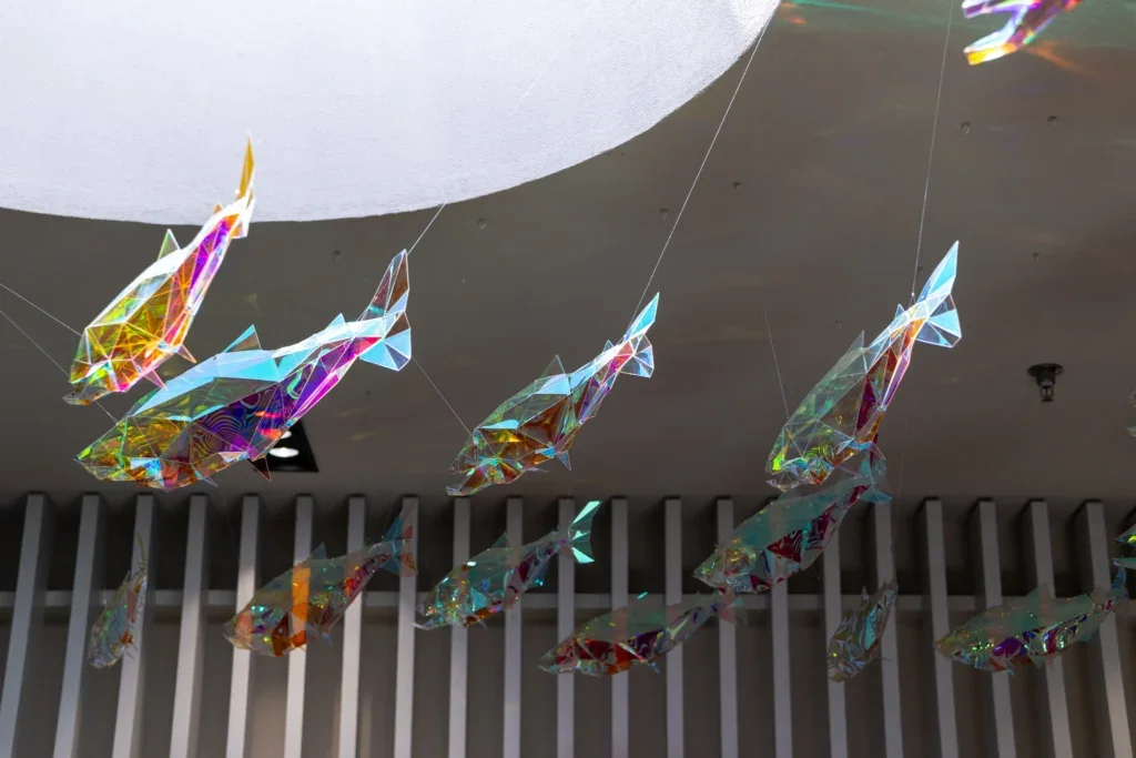 Group of suspended fish sculptures arranged diagonally, with thin support wires visible against ceiling lights.