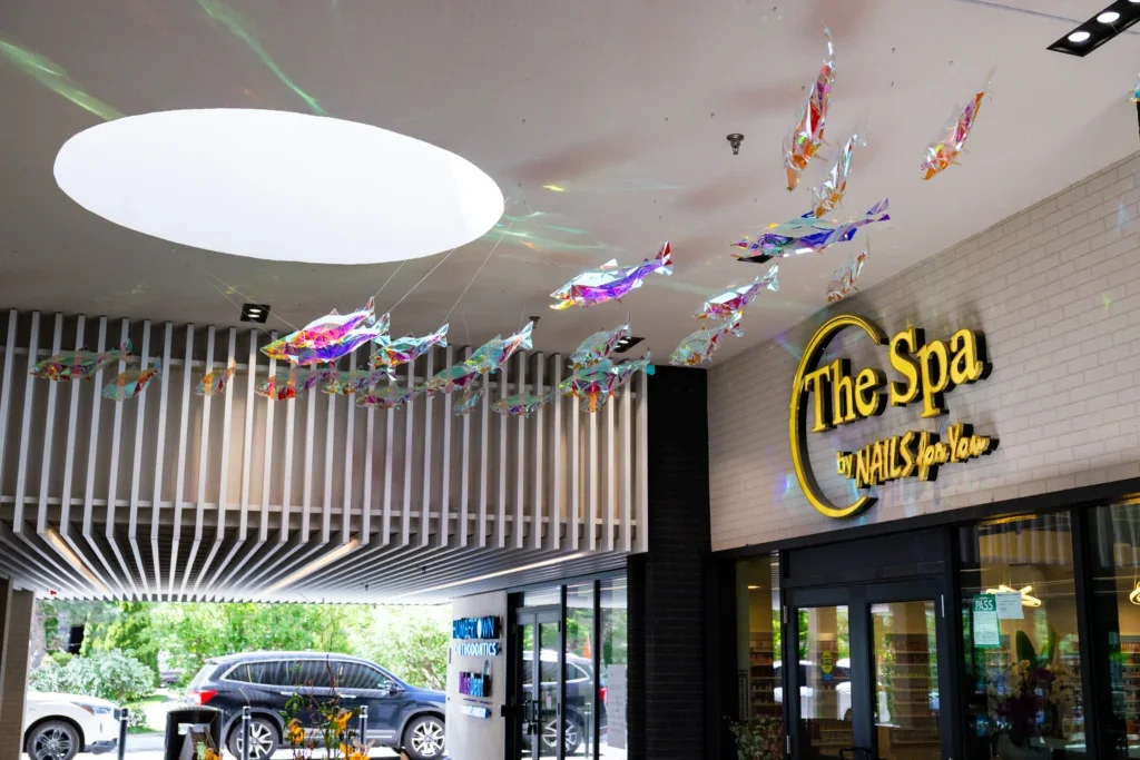 Wide interior view showing suspended fish installation above storefronts, including signage reading “The Spa.”