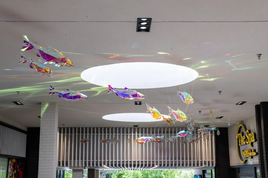 Ceiling view of fish sculptures casting colorful reflections around two circular skylights.